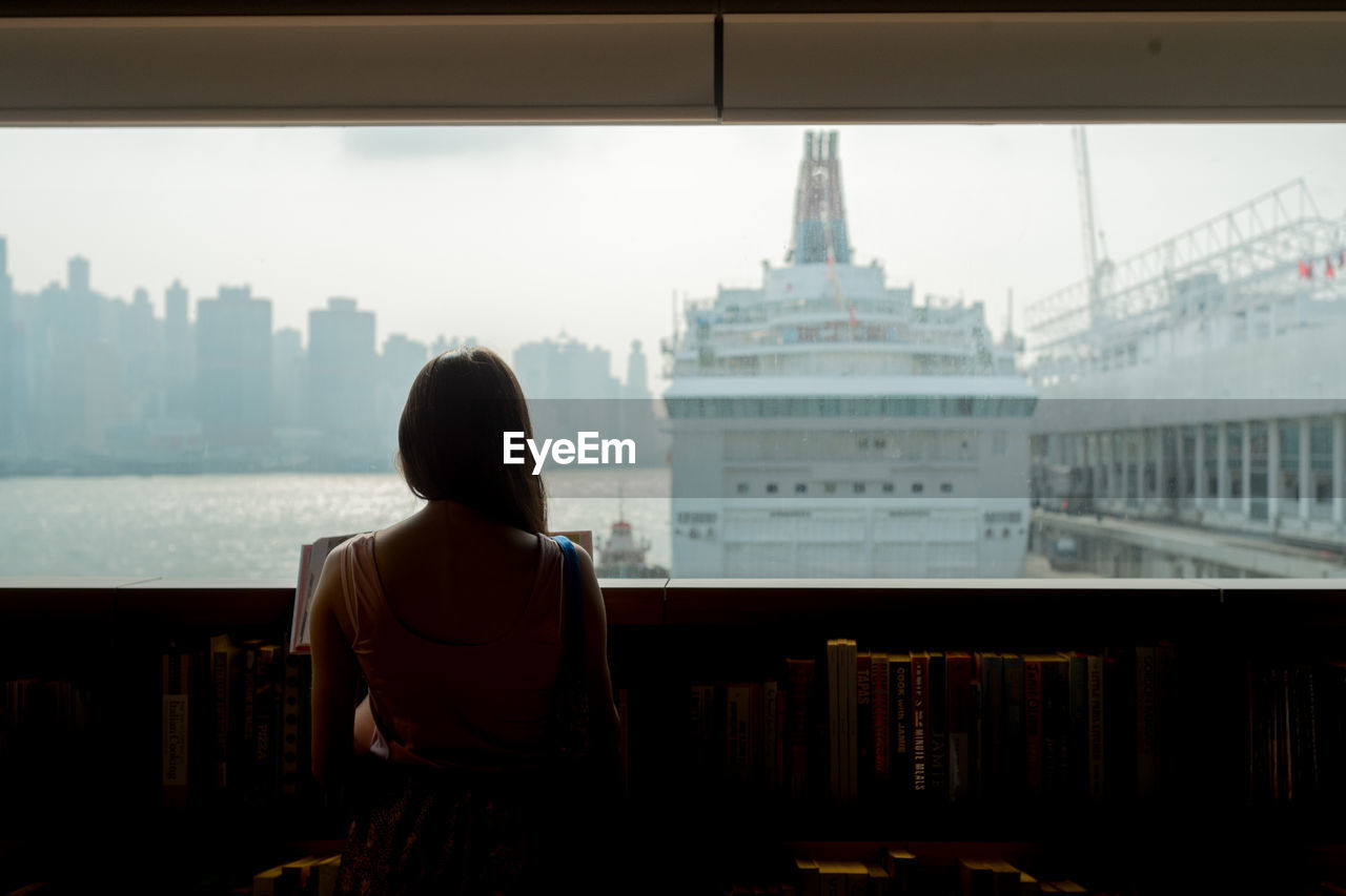 Rear view of woman standing in library against sky