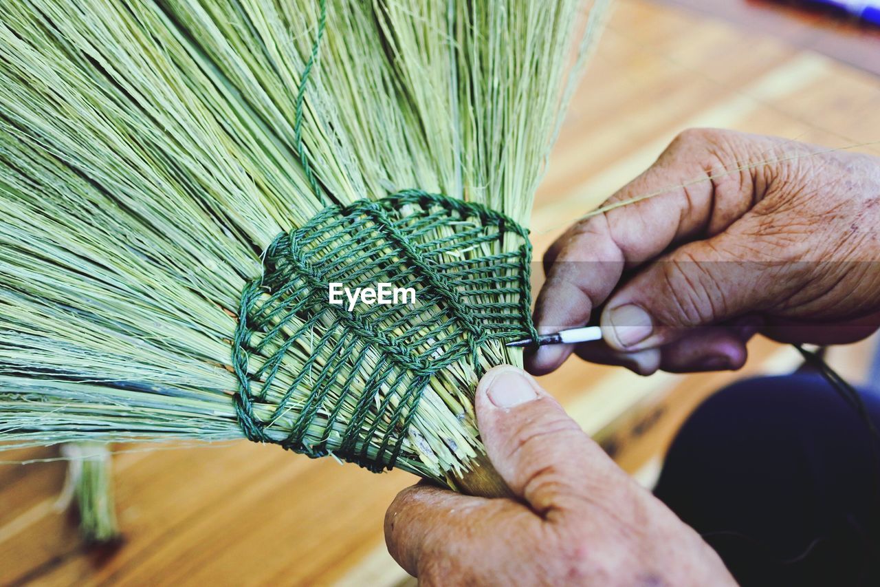 Close-up of cropped hand sewing brooms at workshop