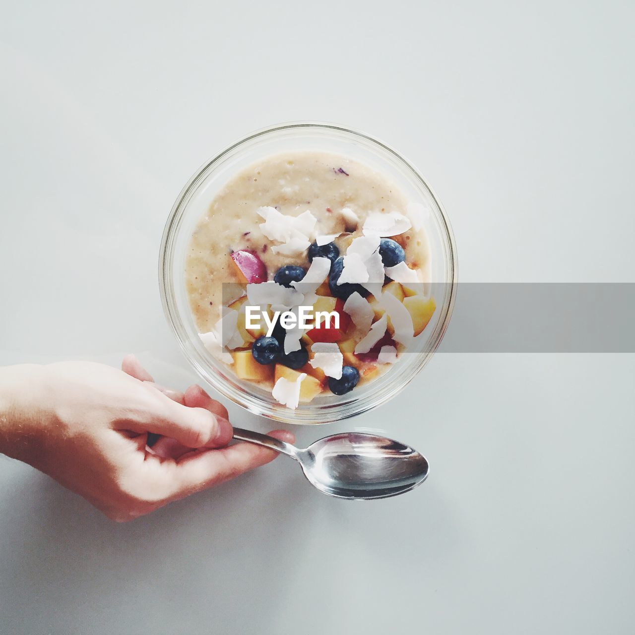 Directly above shot of breakfast cereals with fruits in bowl and cropped hand holding spoon