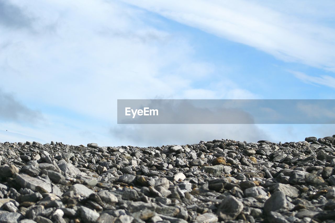 Low angle view of stone covered field against cloudy sky