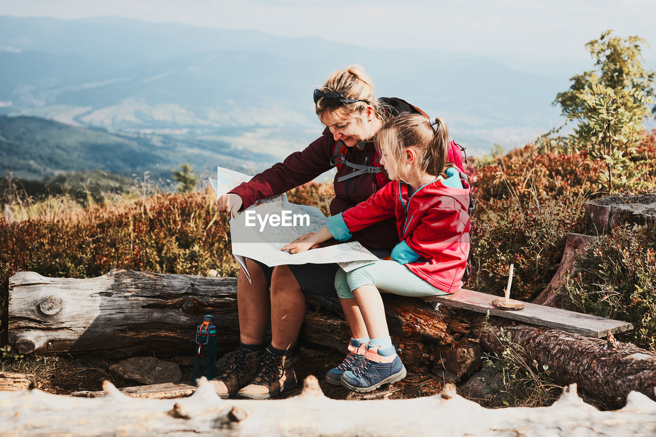 Family trip in mountains. mother and her little daughter examining map, taking break during trip