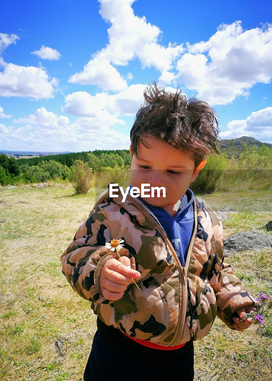 Boy holding flower while standing on grassy field