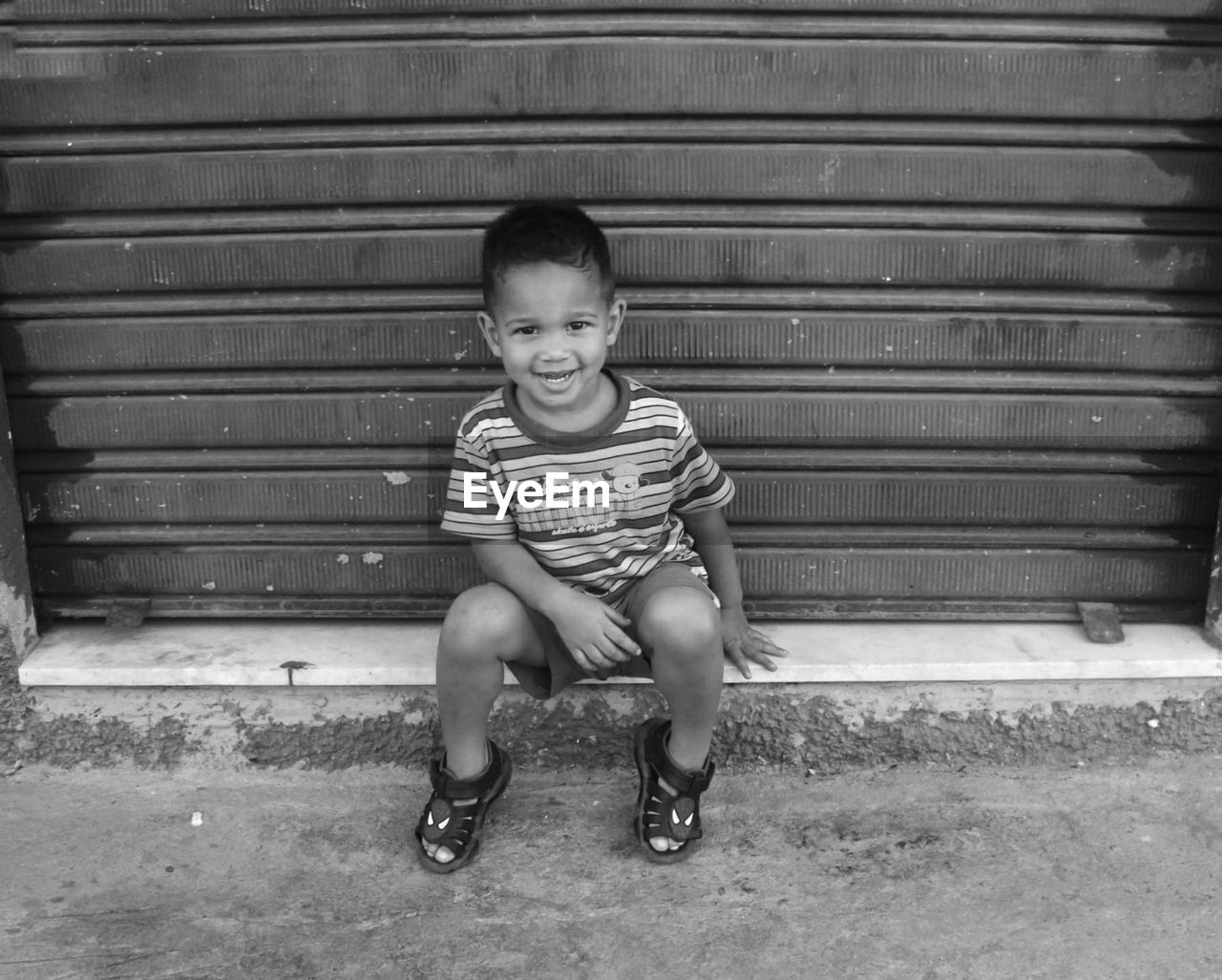 Portrait of boy smiling while sitting by closed shutter