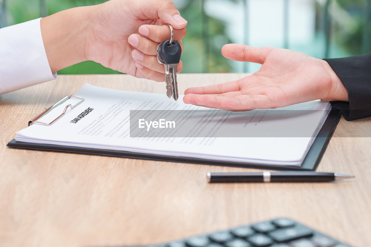 Cropped hand of business person giving keys to colleague at desk in office