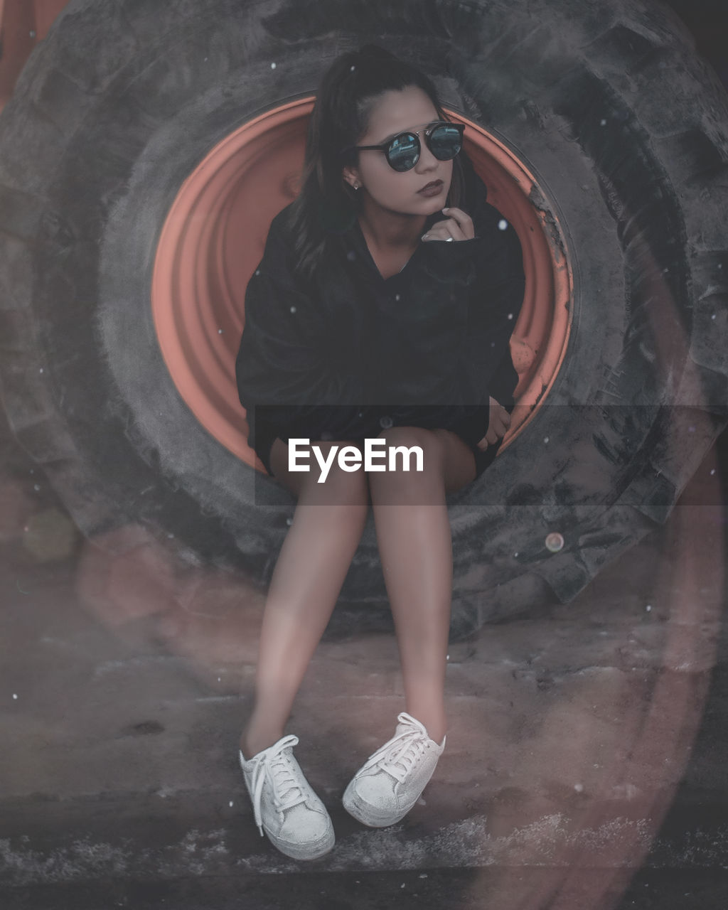 Young woman wearing sunglasses while sitting on tire