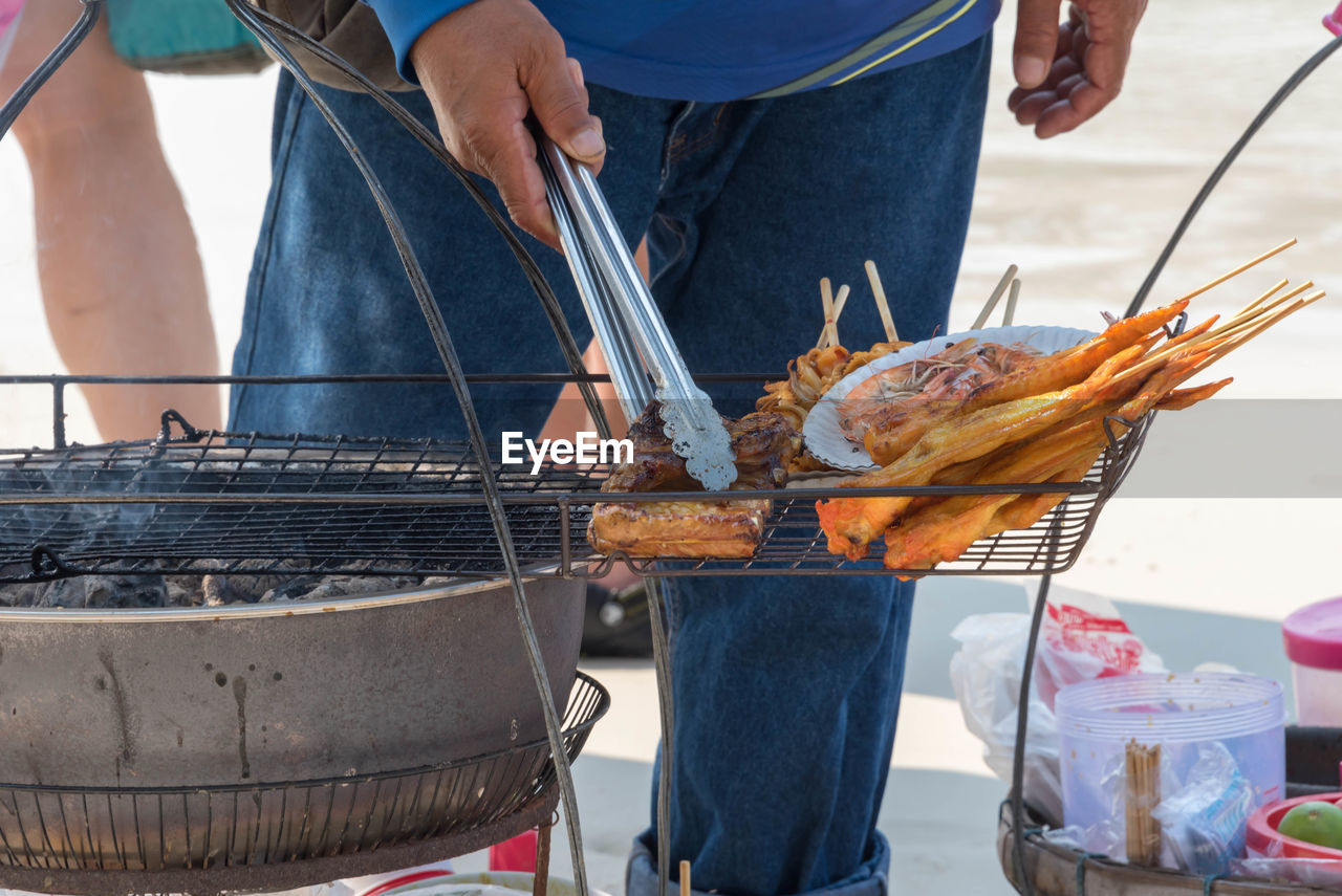 MIDSECTION OF MAN PREPARING FOOD ON BARBECUE