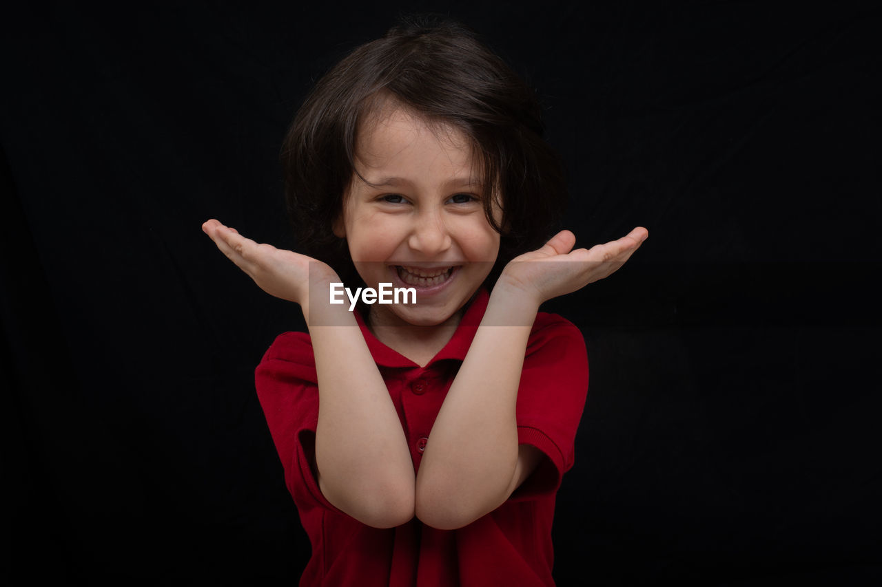 Close-up portrait of cheerful boy gesturing against black background