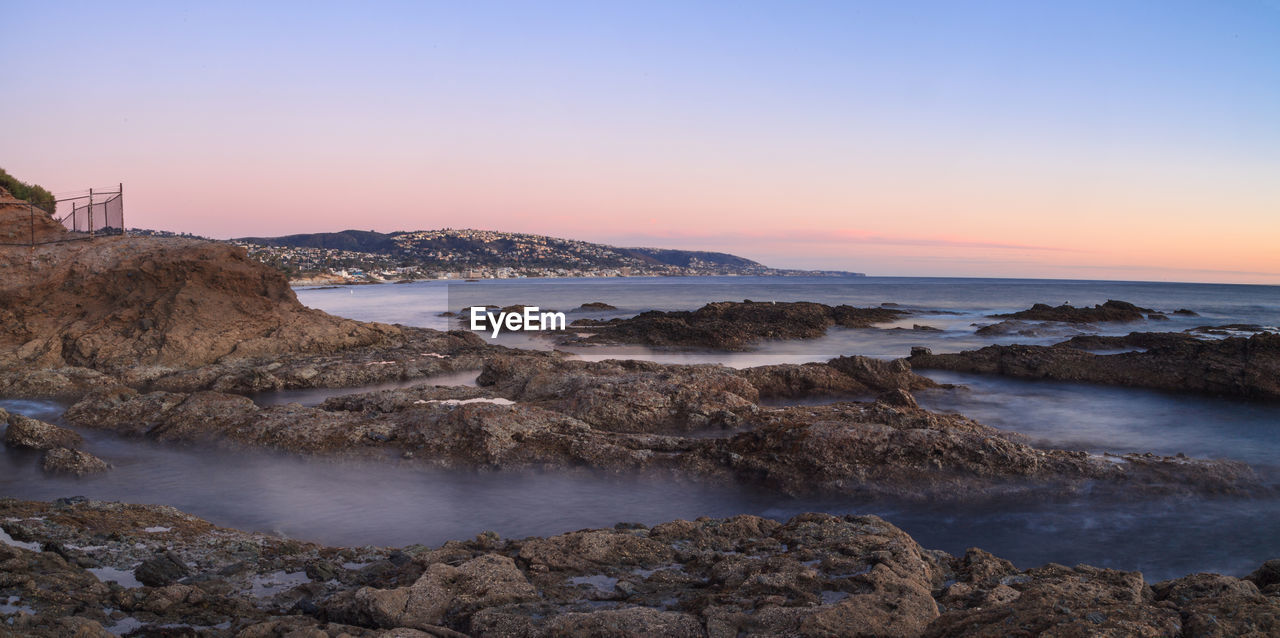 Scenic view of rocky shore against sky during sunset 