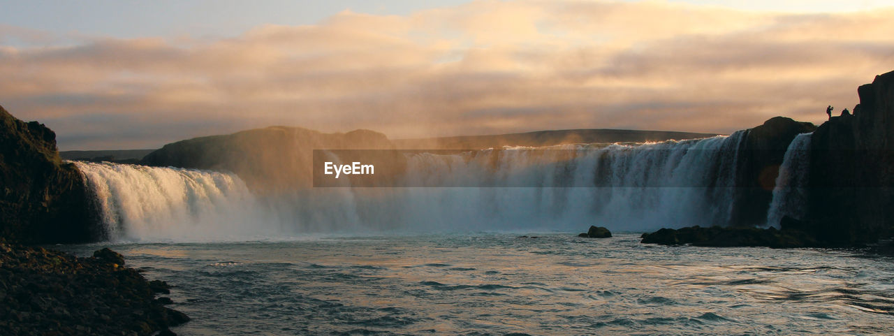 Scenic view of waterfall against cloudy sky at sunset