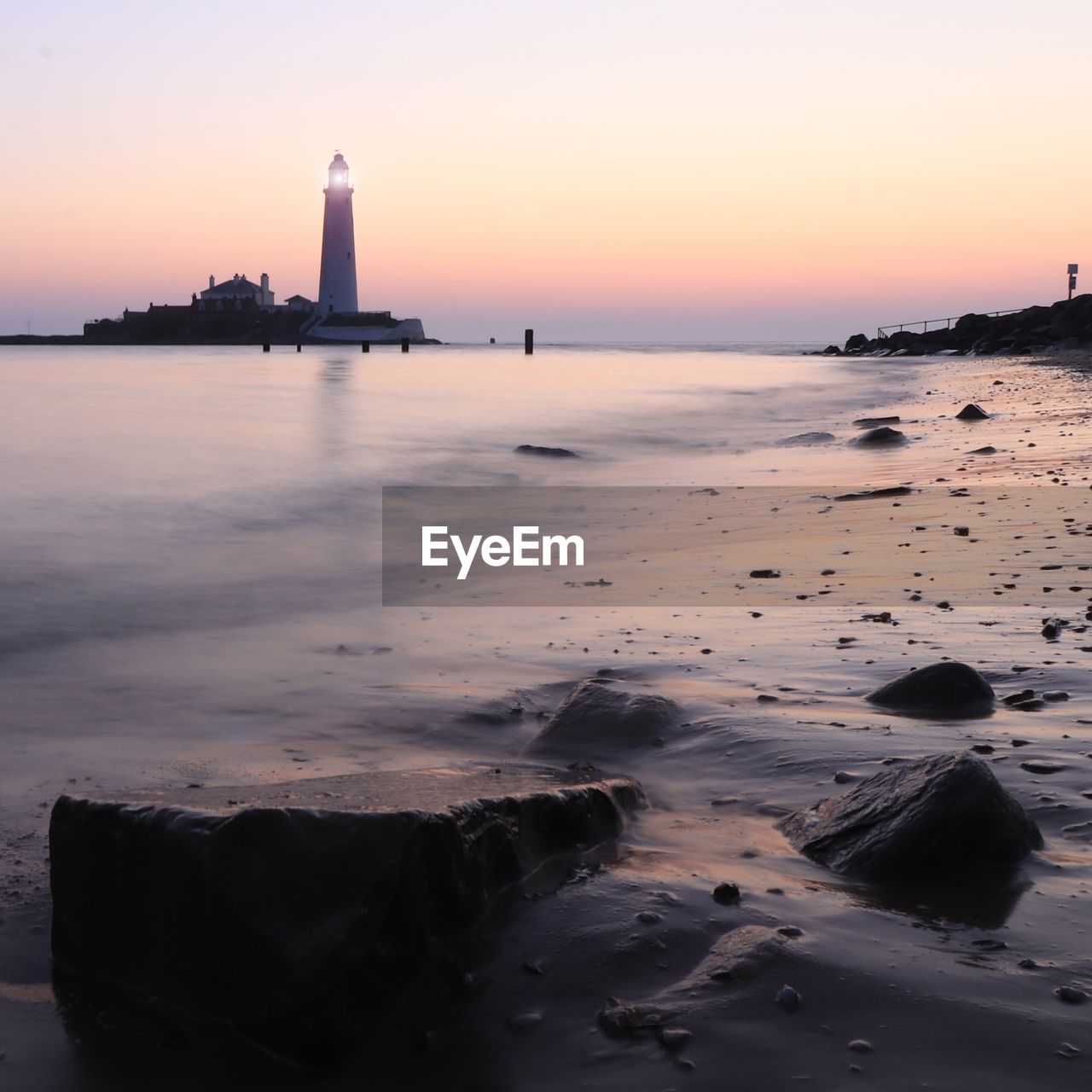 Lighthouse by sea against sky during sunset