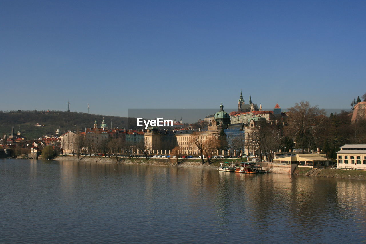 BUILDINGS BY RIVER AGAINST CLEAR BLUE SKY