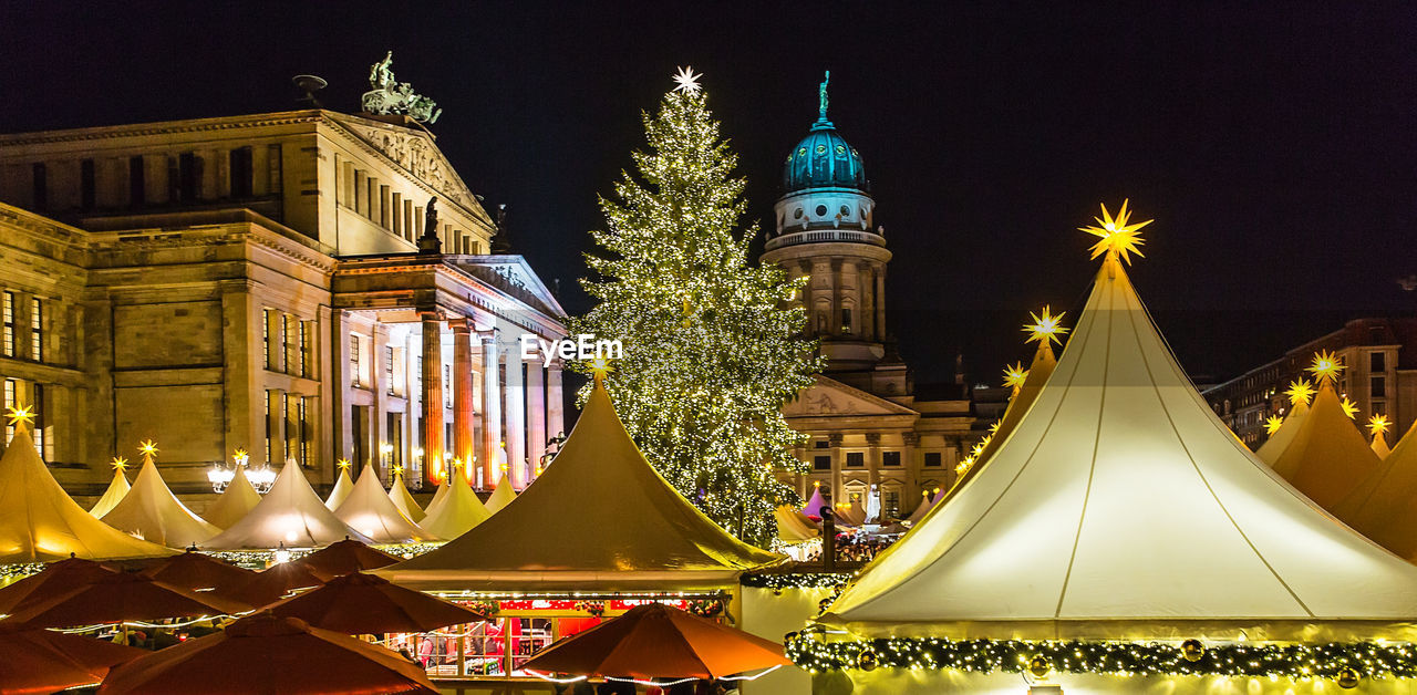 Illuminated tents at night market in city against sky during christmas