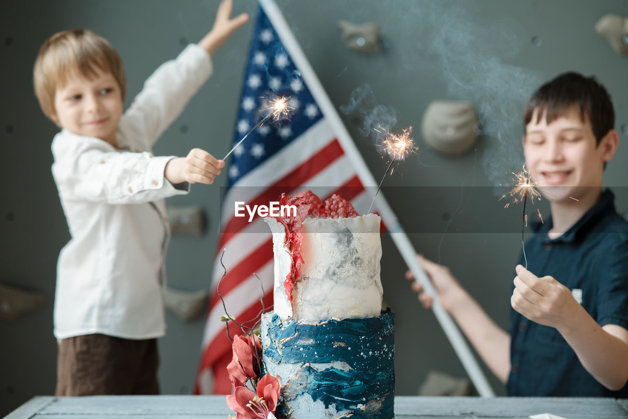 Smiling kids holding american flag and lighted sparklers at independence day celebration