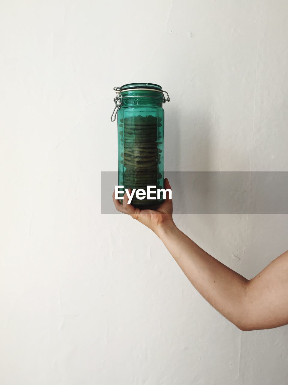 Cropped image of woman holding cookies in jar against wall