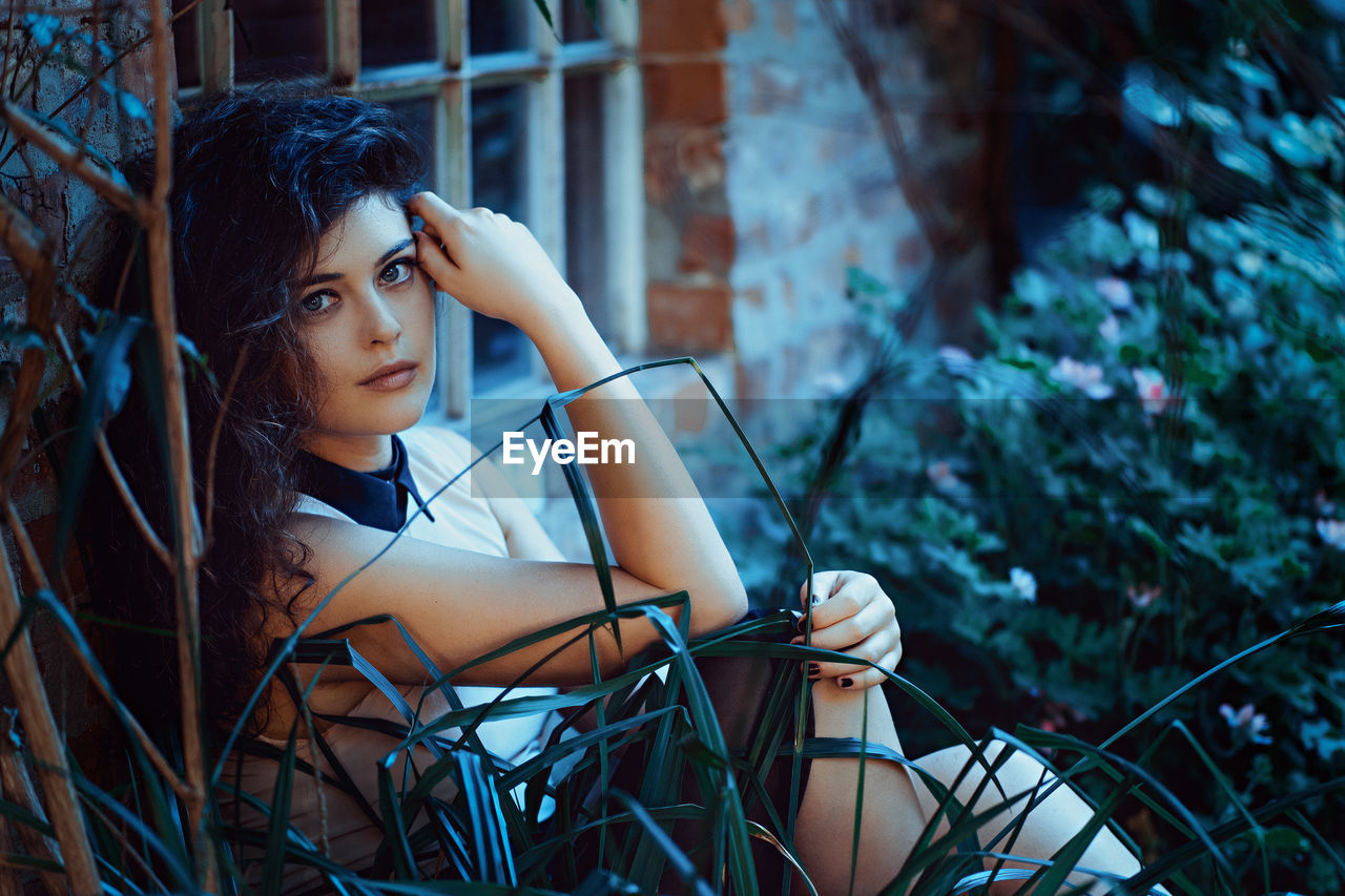 Portrait of beautiful young woman sitting by plants