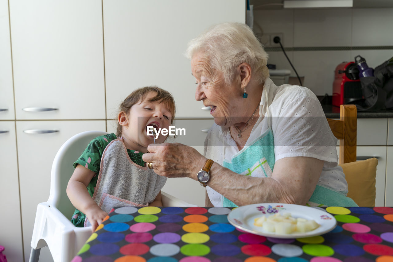 Grandmother feeding granddaughter in the kitchen