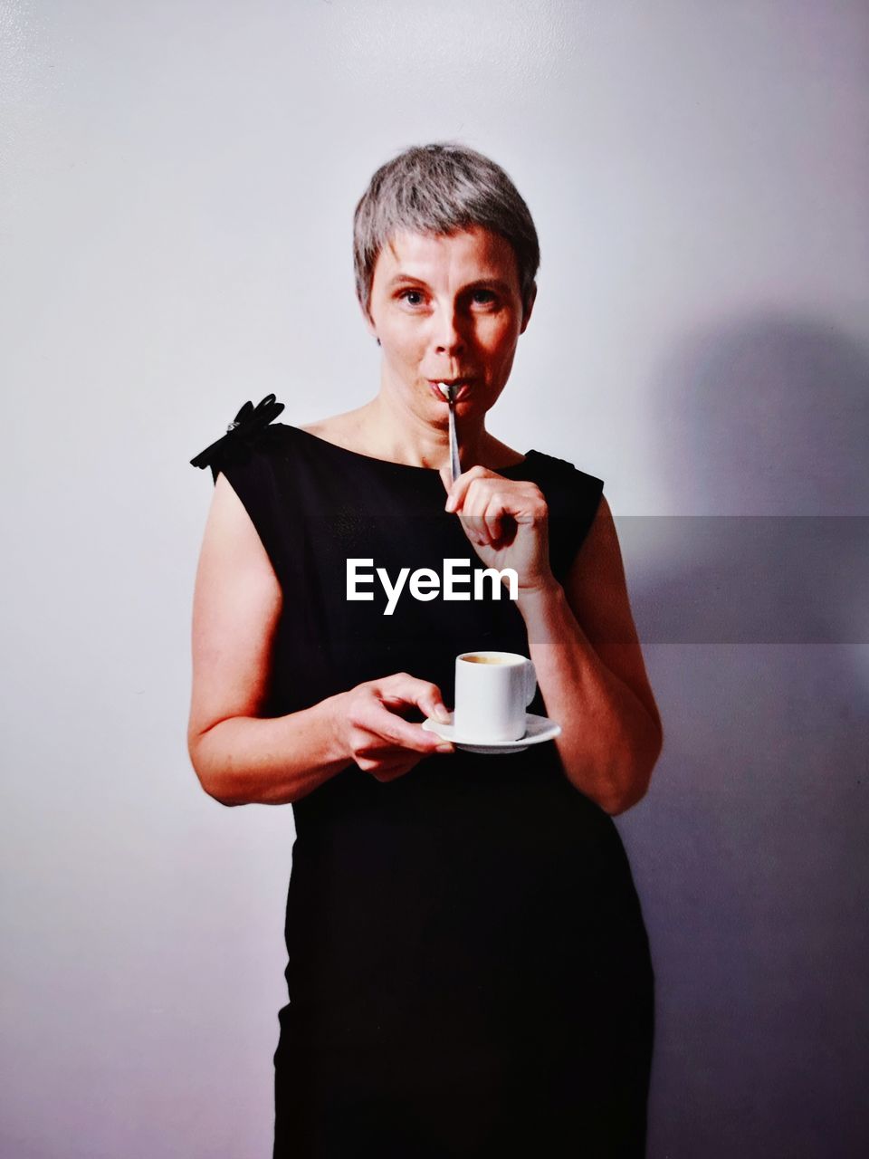 Mature woman holding coffee cup while standing against wall