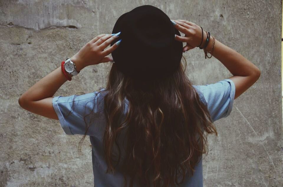 Rear view of teenage girl wearing hat in front of wall