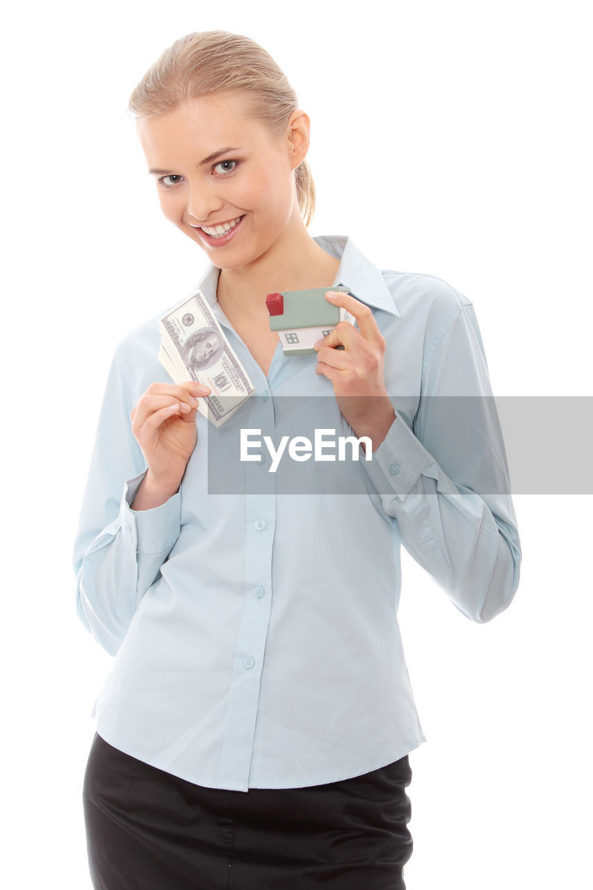 Portrait of real estate agent with papery currency and model home standing against white background