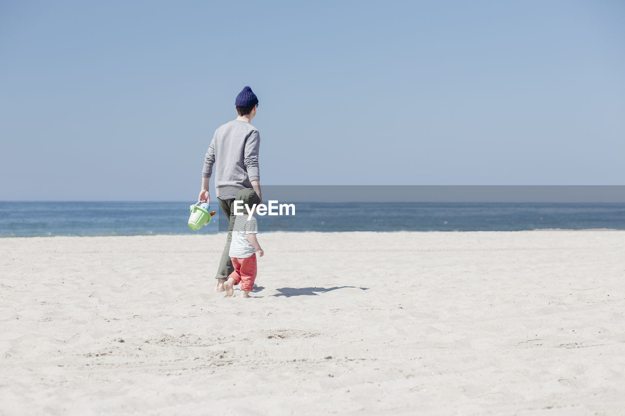 Father and son walking together at beach during sunny day