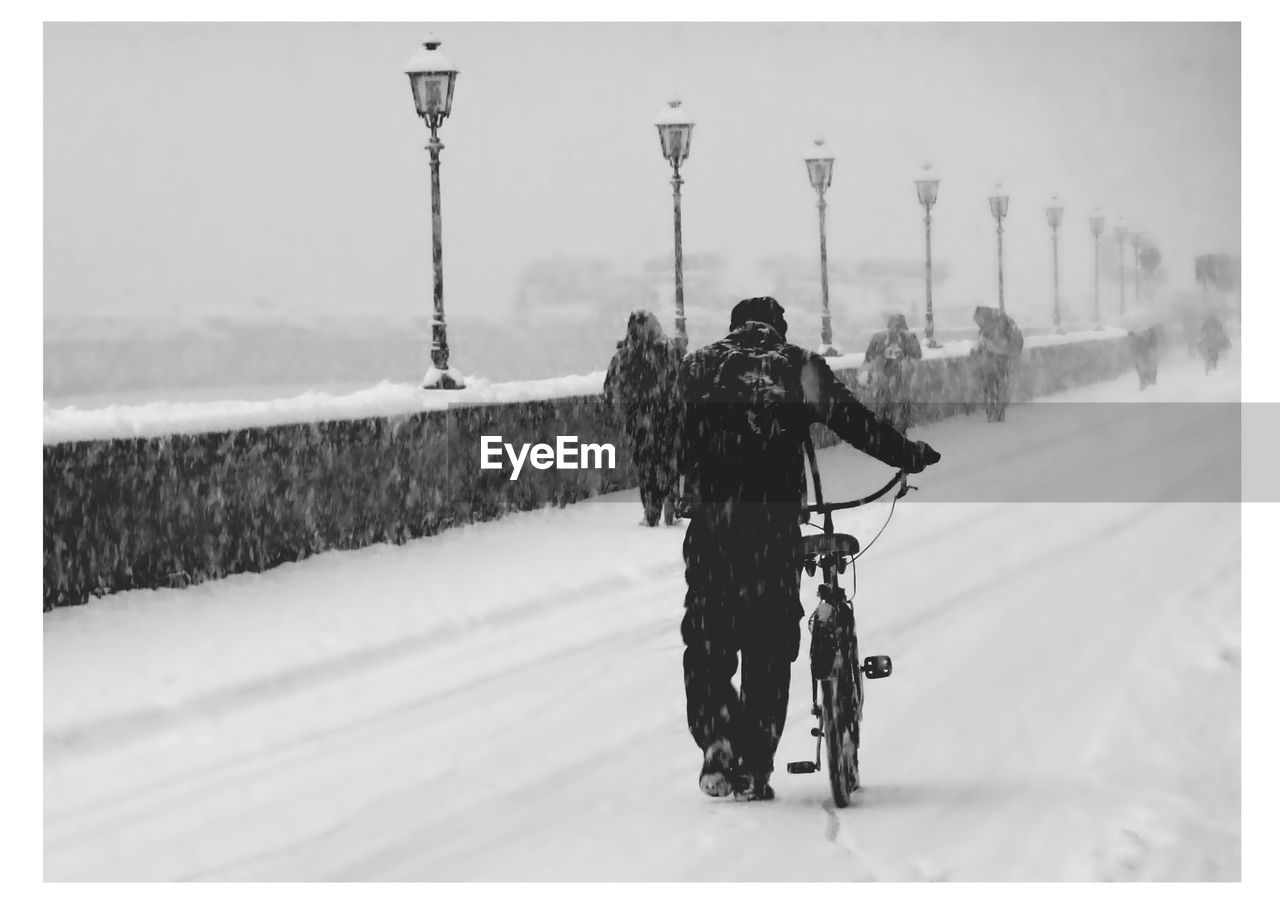 Rear view of man with bicycle walking on snow covered road