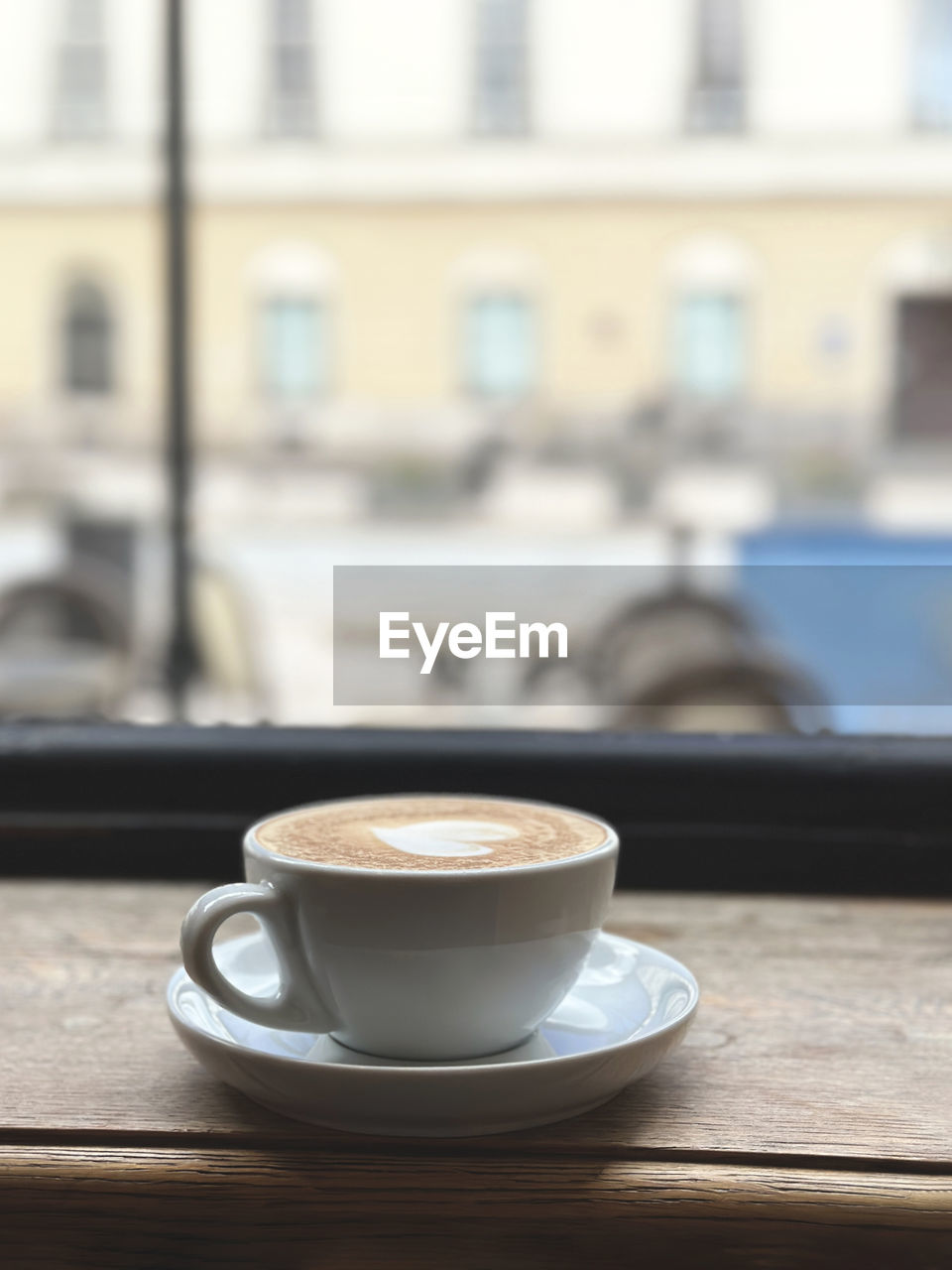 Cappuccino coffee in white cup on wooden table in a cafe with city view.