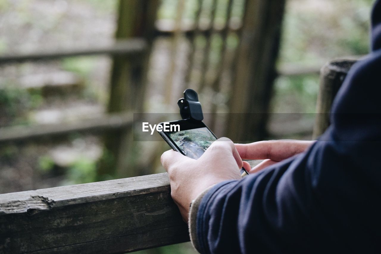 Cropped hands using phone on wooden railing