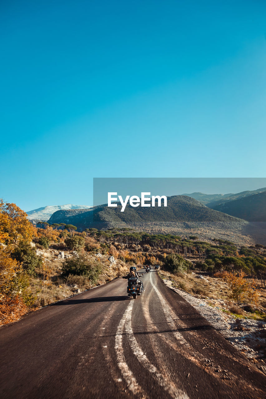 transportation, road, sky, mountain, landscape, environment, nature, scenics - nature, horizon, travel, the way forward, beauty in nature, blue, mode of transportation, mountain range, morning, clear sky, non-urban scene, land, travel destinations, day, copy space, outdoors, tranquil scene, remote, tranquility, journey, sunlight, motion, highway, dusk, tree, infrastructure, no people, plant, road trip, on the move, sunny, motor vehicle, cloud, country road