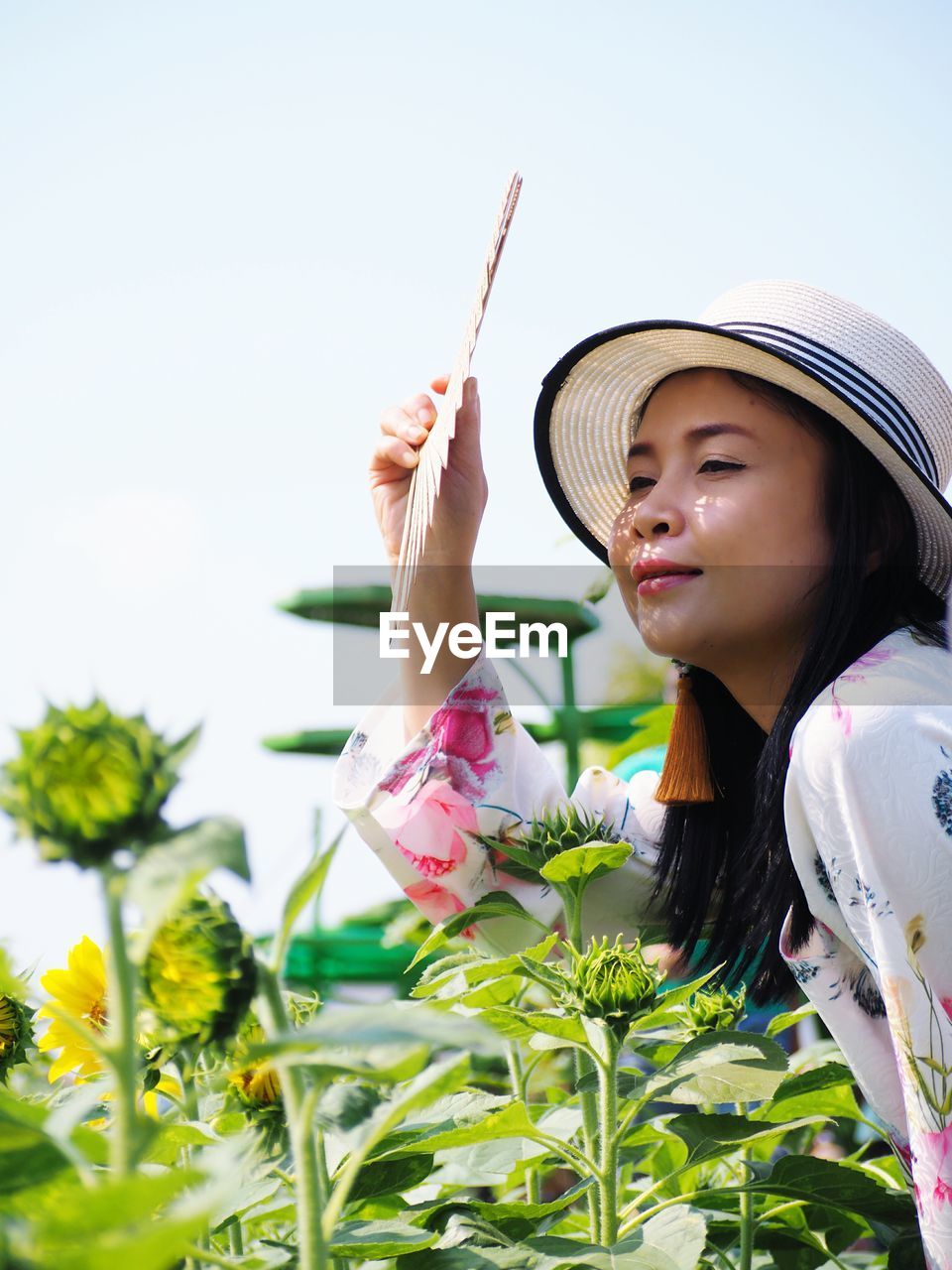 Smiling woman holding hand fan by plants