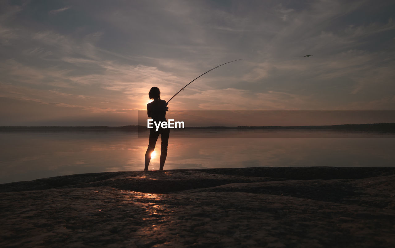 A girl with a fishing rod casts a lure into the lake. back view. scenic atmospheric view. 