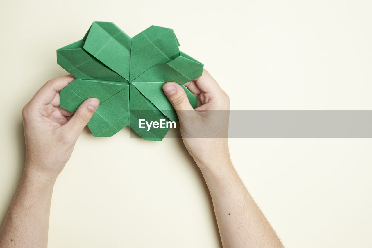 CROPPED IMAGE OF HAND HOLDING PAPER OVER WHITE BACKGROUND