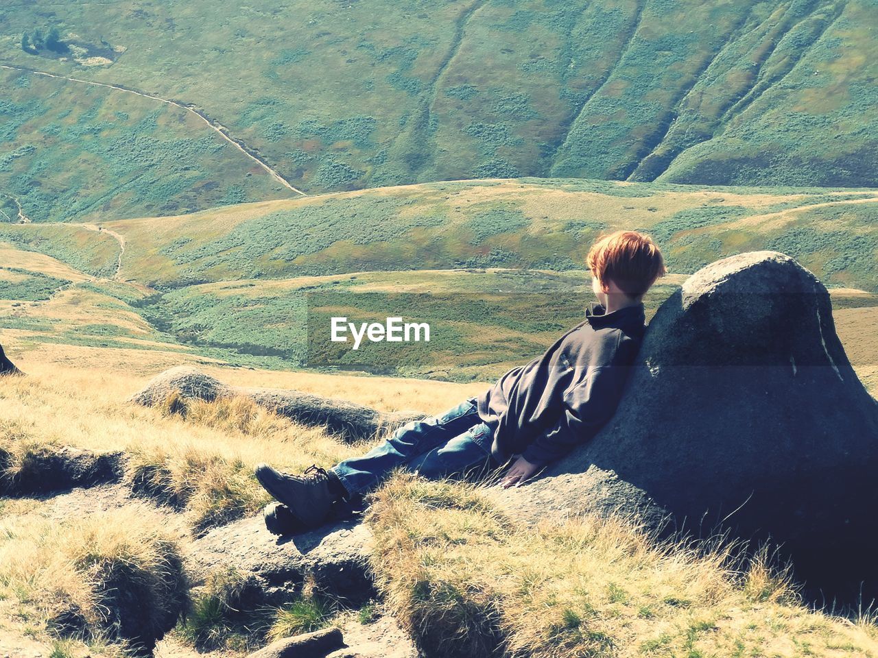 Boy looking away while relaxing on rock