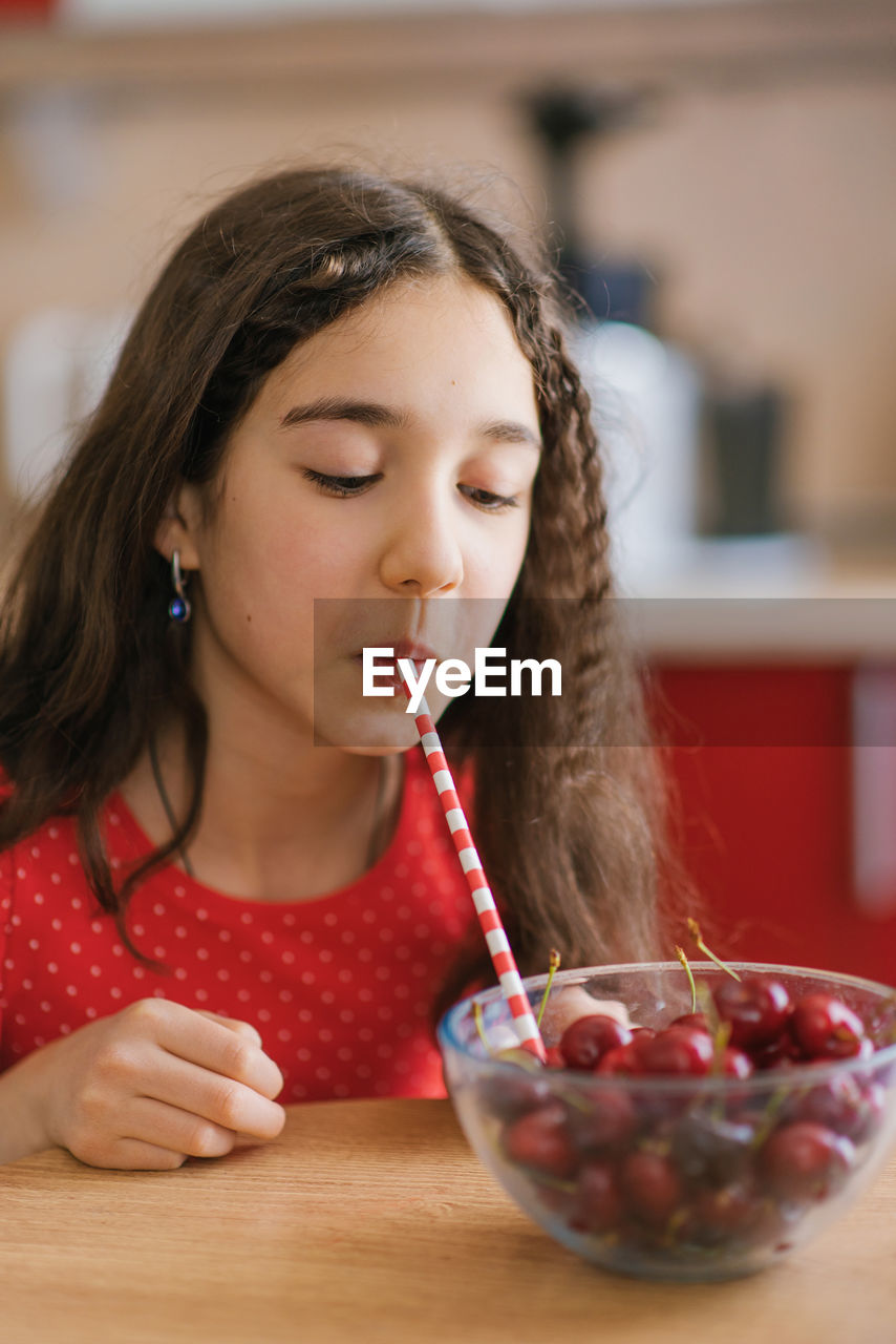 Teenage girl drinks juice from a cherry in a plate through a straw. the concept of an organic drink