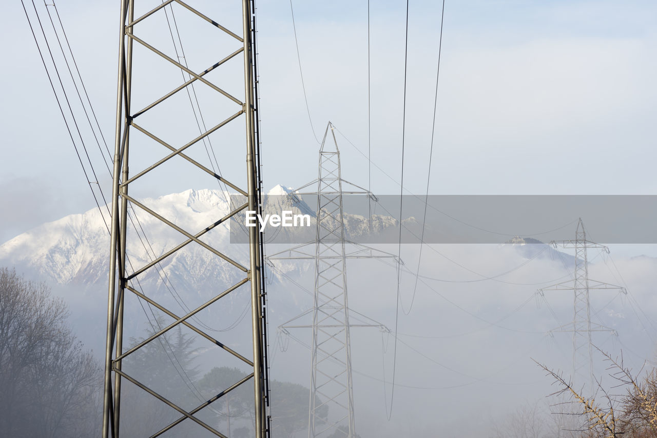 Electricity pylon against snowcapped mountain and sky