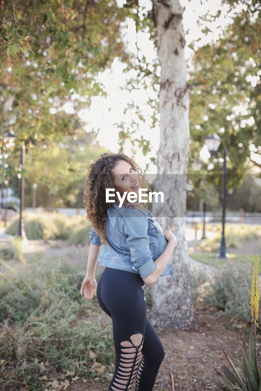 Side view of young woman standing against trees