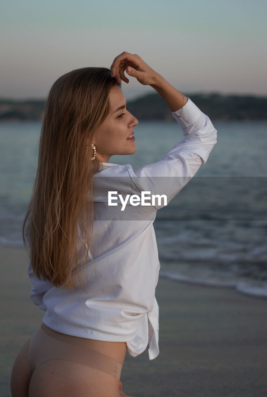 Beautiful woman sitting at beach against sky