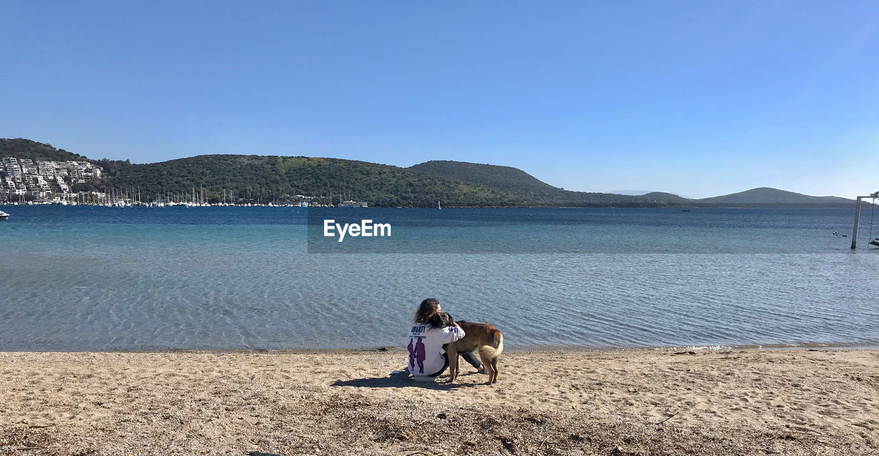 PEOPLE SITTING ON BEACH AGAINST CLEAR SKY