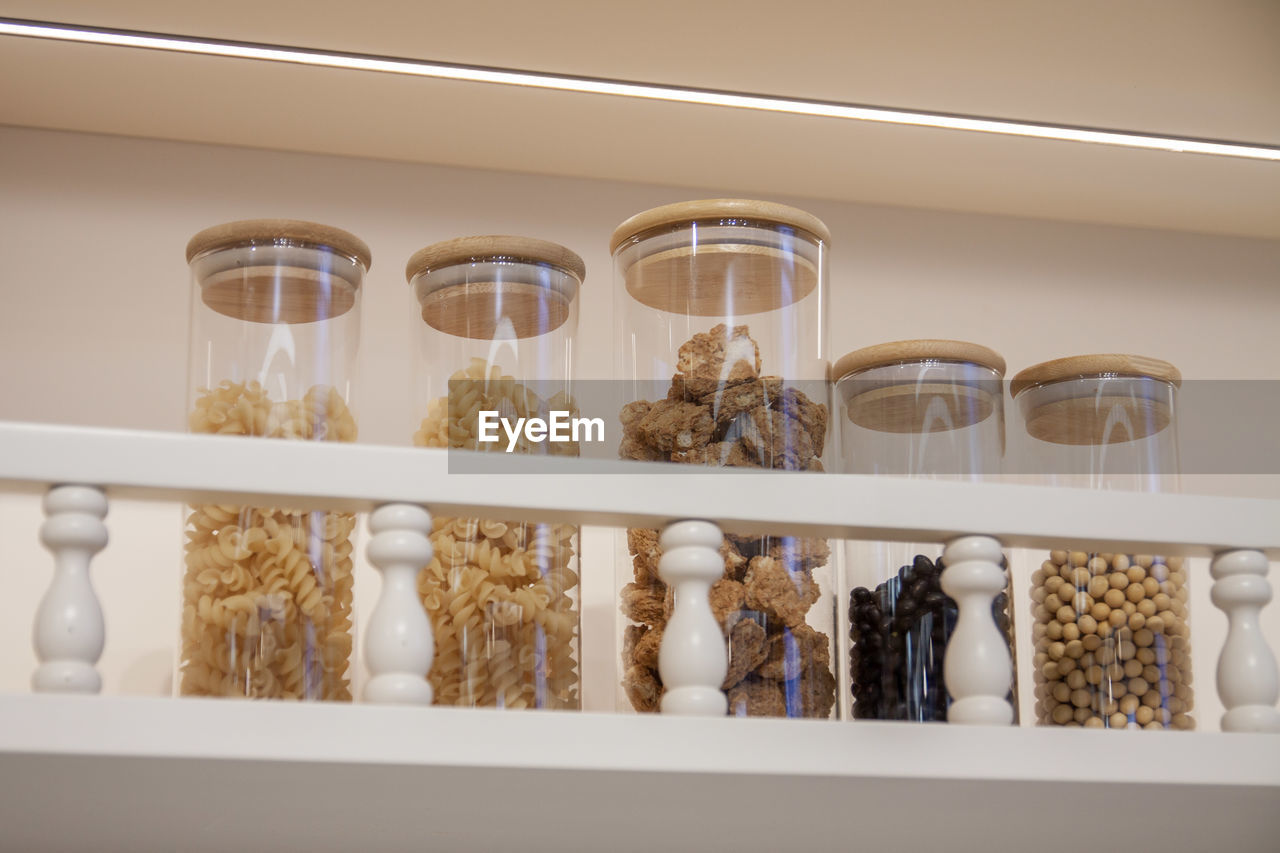 Glass jars of macaroni, nuts and grains on a kitchen shelf