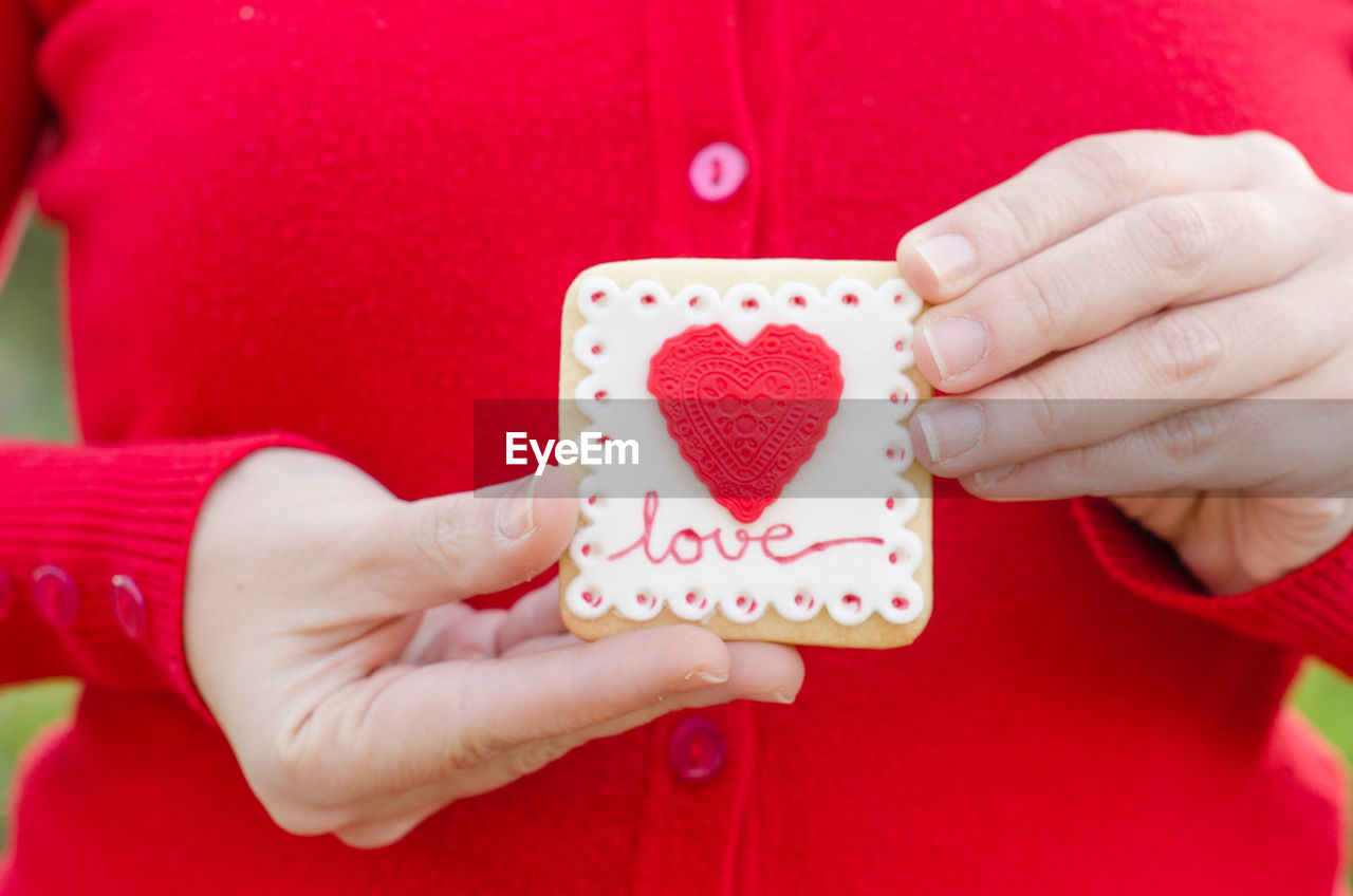 Close-up midsection of woman holding cookie with heart shape