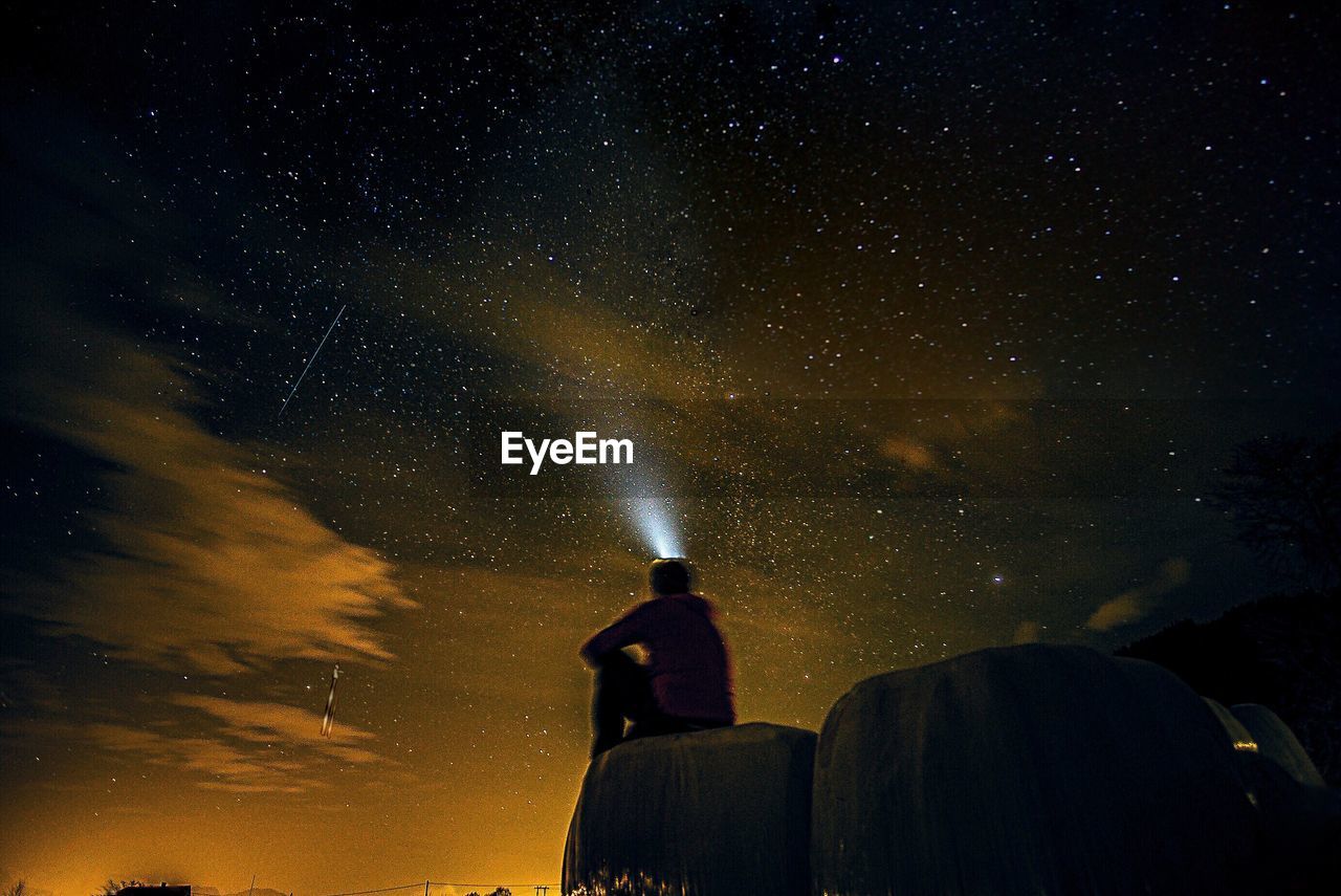 Rear view of man with flashlight against sky at night
