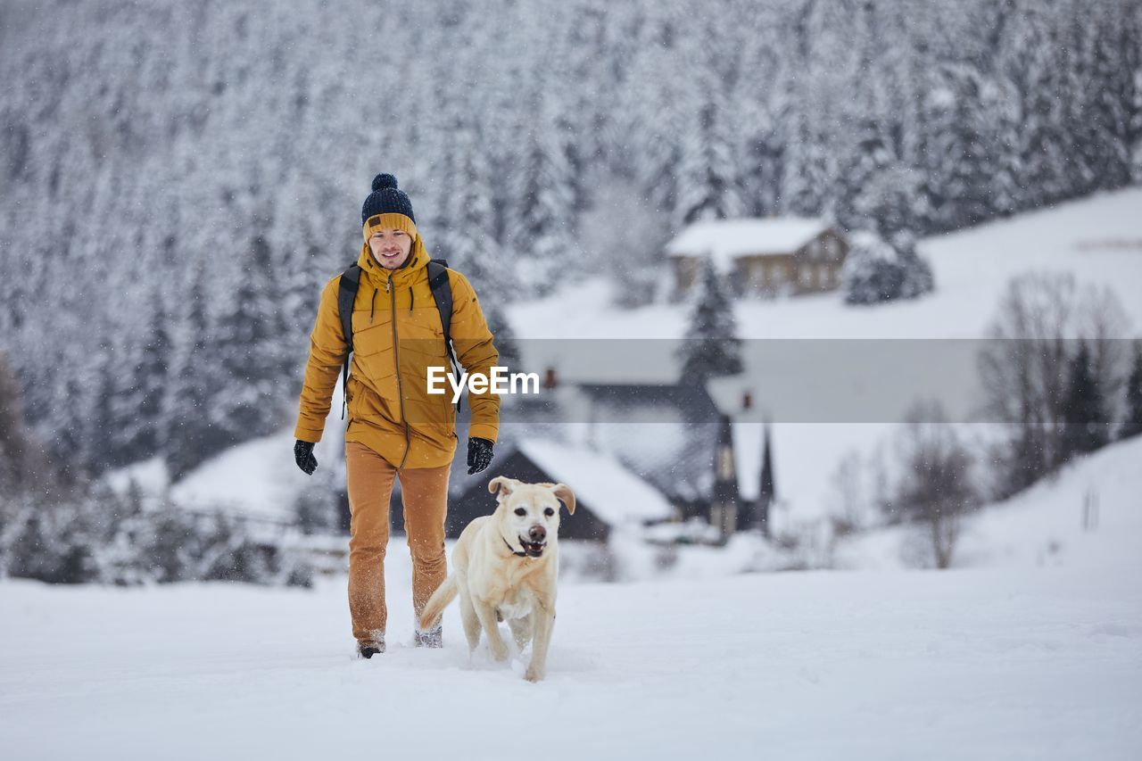 Full length of man walking with dog on snow covered land