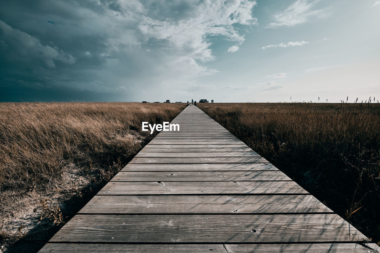 Boardwalk on field against sky