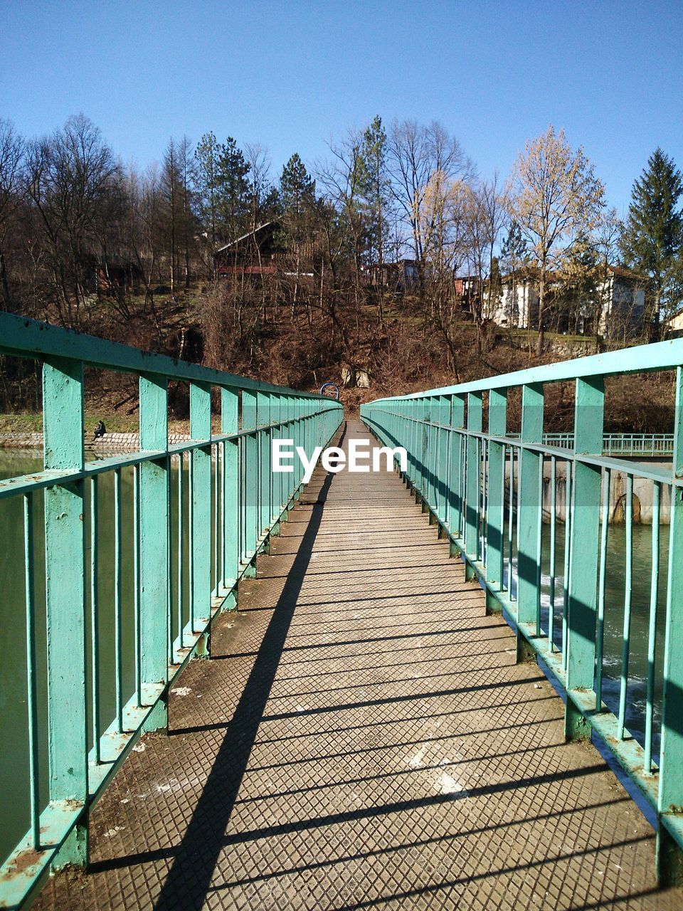 Narrow footbridge with railings against trees