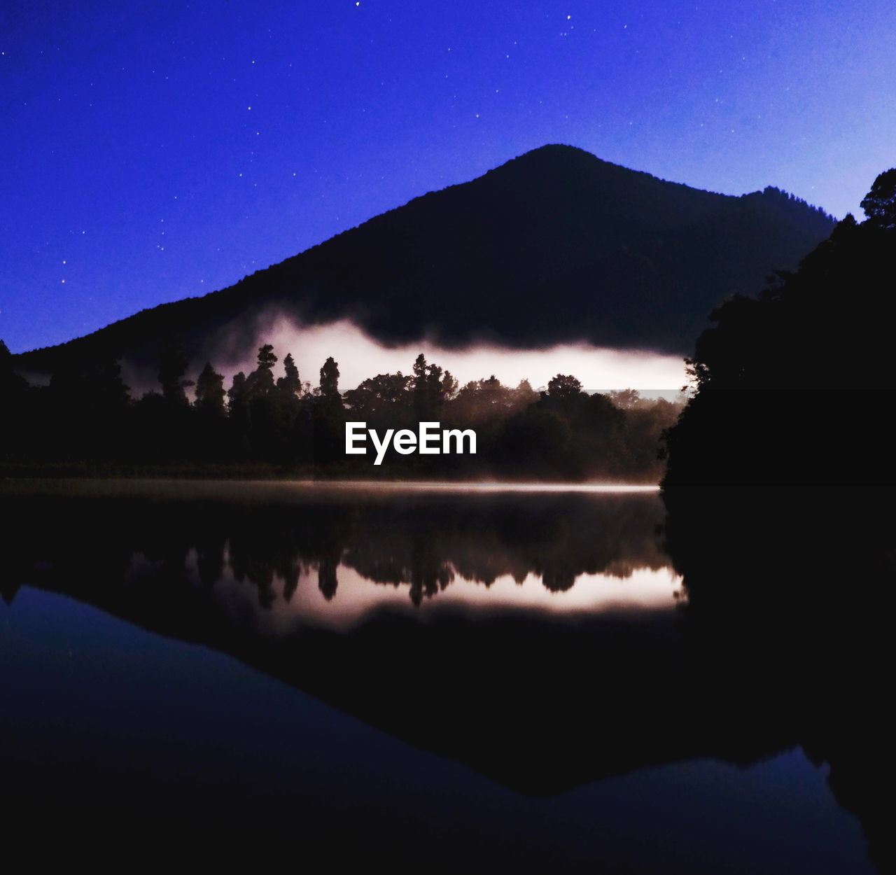 REFLECTION OF SILHOUETTE TREES IN LAKE AGAINST SKY