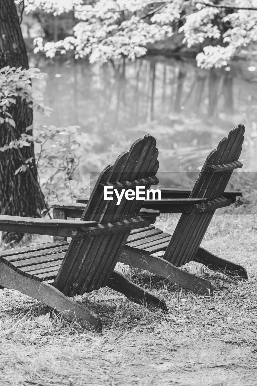 Empty adirondack chairs by pond in forest