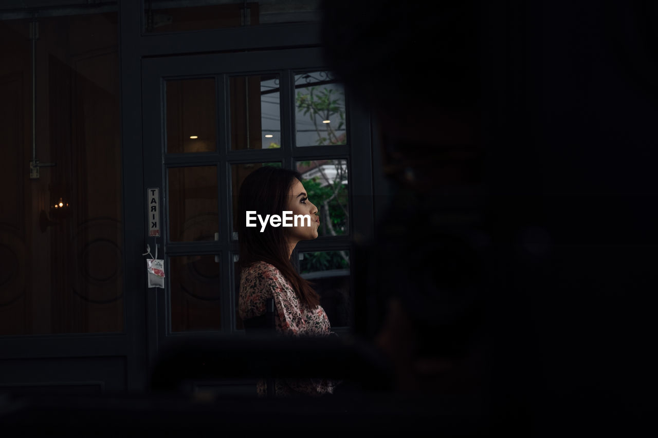 Side view of young woman puckering lips seen through window