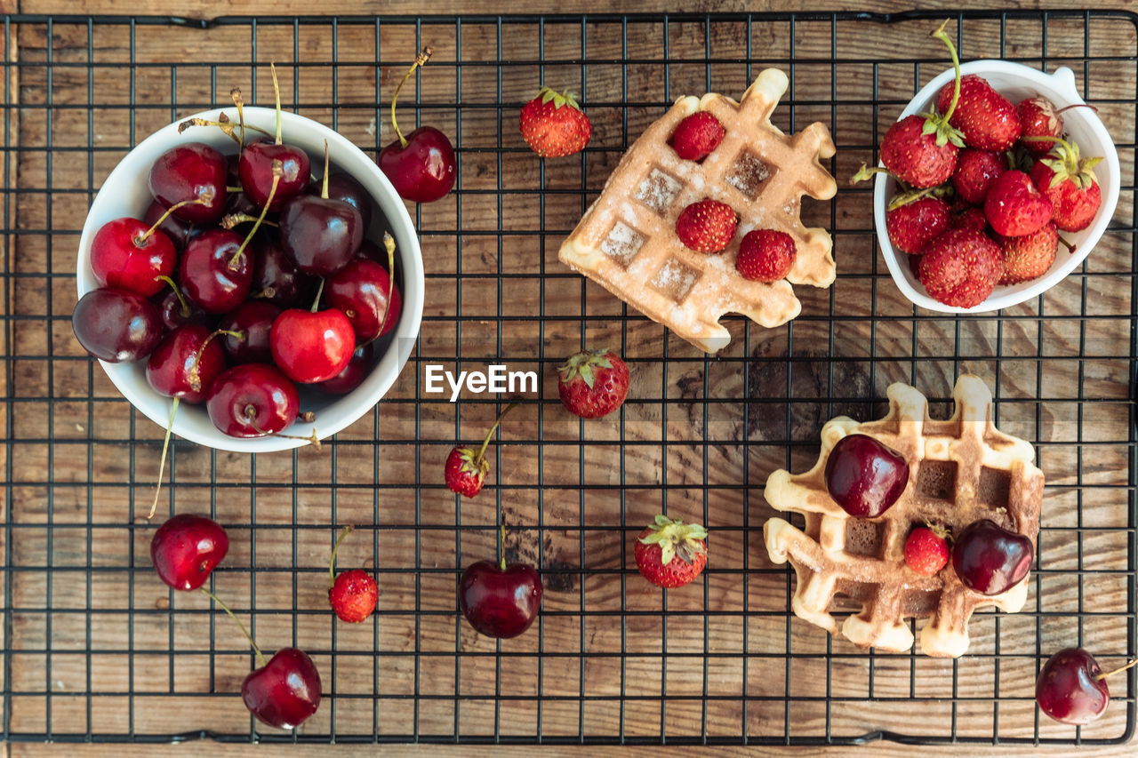 Fresh cherries in a bowl and strawberries with viennese waffles on a wooden table top view