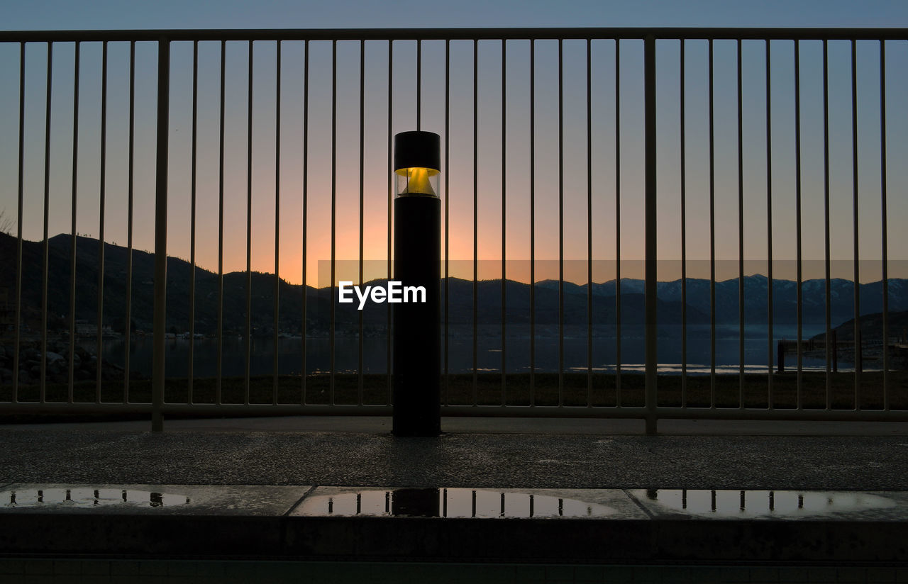 Illuminated bollard by railing against mountains during sunset