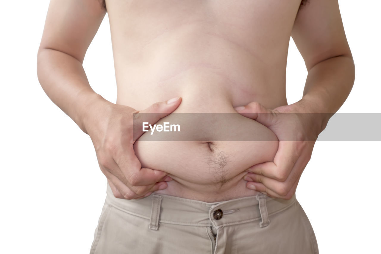 Midsection of overweight man holding abdomen while standing against white background