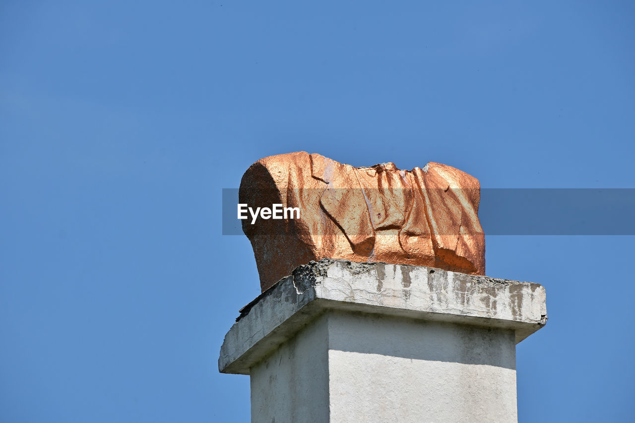 Low angle view of broken bust monument against clear blue sky